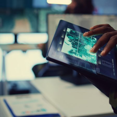 Military IT professional gathers intelligence from world map projection, tablet connected to satellite reconnaissance system to support field troops. Dispatch army command post. Close up. Camera B.