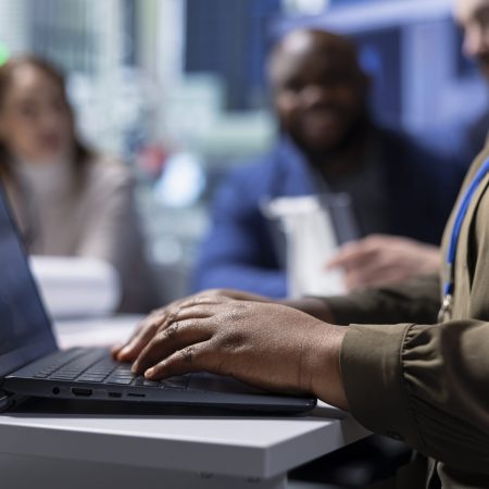 Photovoltaics factory worker analyzing data, reviewing system health metrics with laptop. Solar panels manufacturing plant employee troubleshooting technical issues using notebook, close up